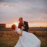 Deux mariés dans un champ au couché du soleil, le marié renversant la mariée de manière légère