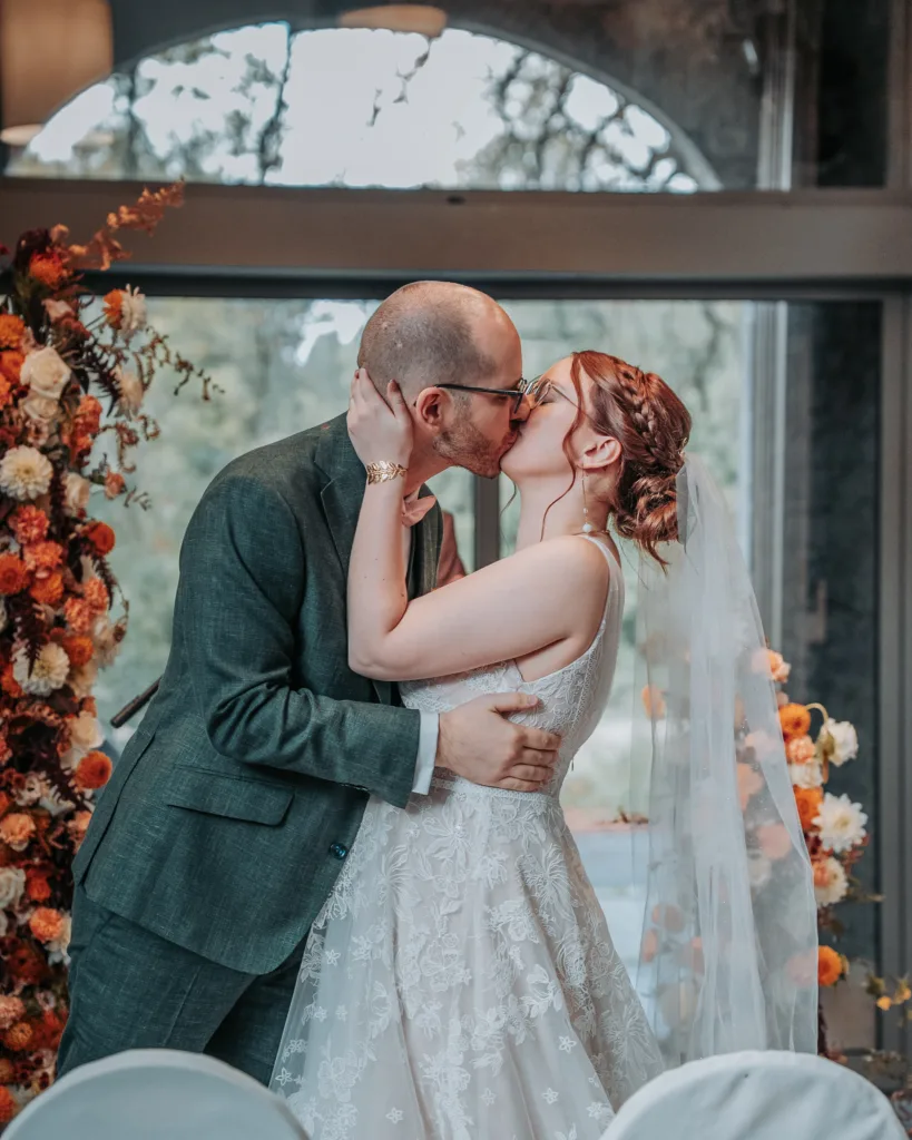 deux mariés s'embrassant devant l'arche de fleurs